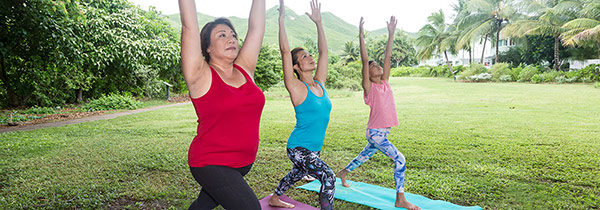 Three women are performing the sun salutation yoga pose.